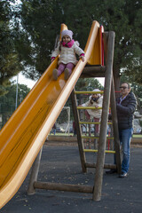 Ritratto di due sorelle gemelle di tre anni mentre giocano al parco con il papà.