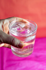 Hand holding glass with ice against pink background