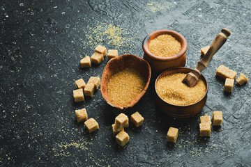 Obraz na płótnie Canvas Brown cane sugar in a bowl. Set of sugar. On a black stone background. Rustic style.