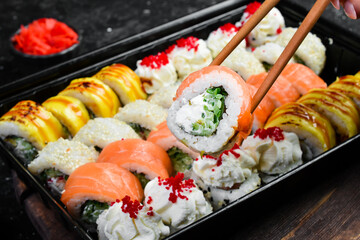 A sushi roll with seafood is held with chopsticks. On a black stone background.