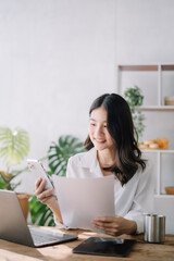 Asian businesswoman  talking mobile phone and working on laptop and papers on table in her office.