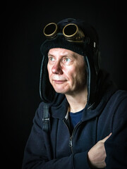 Warmly dressed caucasian man with protective antique glasses on fur trapper hat againgst dark background