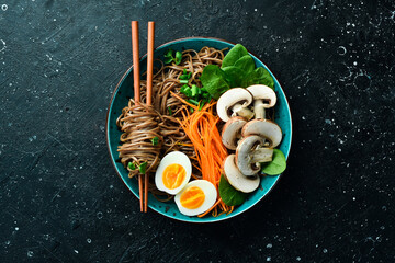 A bowl of soba noodles with mushrooms, onions and egg. On a stone background. Top view.
