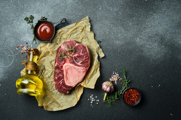 Raw ossobuco steak with rosemary and spices on a black stone background. Free space for text.