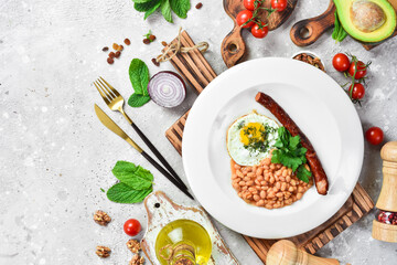 Breakfast. Eggs with sausage and beans. On a white plate. On a gray stone background. Restaurant menu.