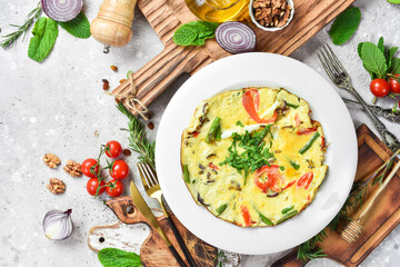Breakfast. Omelette with cheese and vegetables. On a white plate. On a gray stone background. Restaurant menu.