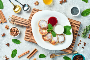breakfast Cheese pancakes with sour cream, jam and mint. On a white plate. On a gray stone background. Restaurant menu.