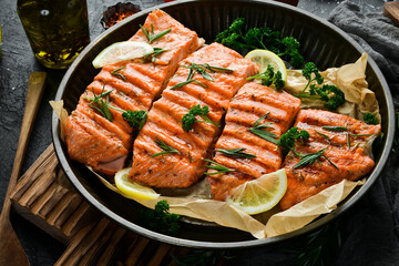 Grilled salmon fillet with spices, lemon and vegetables. On a black background.