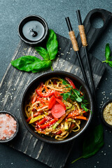 Udon pasta with vegetables and ginger. In a black plate. Japanese cuisine. On a dark background, close-up.