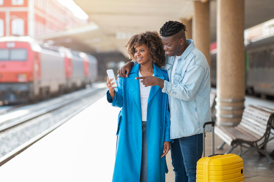 Black Couple Standing At Railway Station And Using Smartphone With GPS Navigation