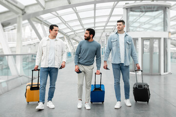 Three Male Tourists With Suitcases Walking In Terminal In Airport