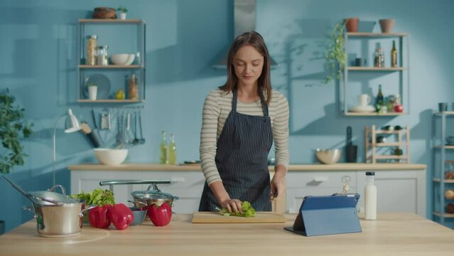 Smiling Woman Preparing Vegetable Meal and Watch Recipes on Tablets in Internet.Vegetarian Woman Cooking Healthy Food Salad Using Cookbook. Lifestyle, On-line Recipes, Food Delivery Services Concept.