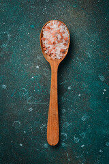 Fototapeta na wymiar Sea kitchen pink coarse salt in a wooden spoon. On a dark textured background.