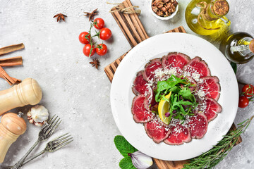 Veal carpaccio with lemon and arugula. On a white plate. On a gray stone background. Restaurant menu.
