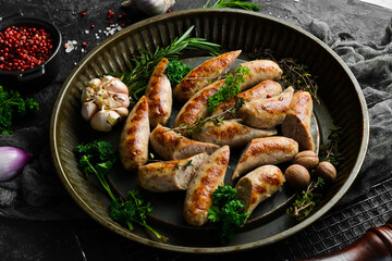 Grilled sausages with rosemary and spices. Barbecue. On a black stone background.