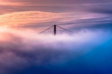 Sunset over Golden Gate Bridge from Alcatraz Island lost in mist. Close-up of tower and cables...