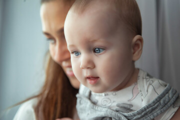 Adorable newborn baby on hands loving happy mom at home, looking away. Mother with kid together in living room. Mom care 6 months old infant child. Concept of motherhood, maternity. Copy ad text space