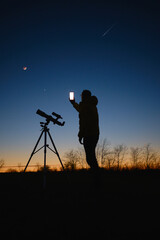 Astronomer looking at the starry skies with planets, falling stars and Moon eclipse with a...