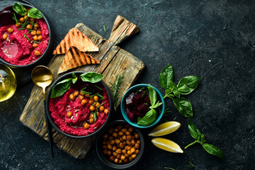 Beetroot chickpea hummus in a bowl. Red hummus. Healthy vegetarian food. On a concrete black background.