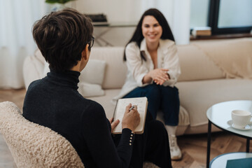 Psychologist writing down notes during therapy session with smiling woman - 591170261