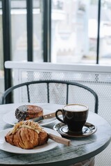 Portrait or Vertical Shot of Breakfast Set: Almond Croissant, Chocolate Crombolomi, and a Cup of Coffee on a Wooden Table. Focus on the Cup of Coffee.
