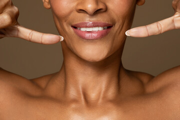 Oral care. Black middle aged woman pointing at her smile, showing white teeth, standing over brown...