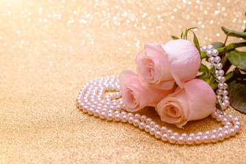 Pink rose and pearl necklace on a shiny gold background
