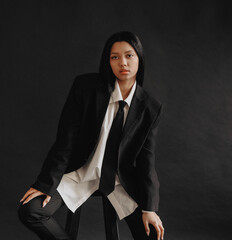 A young African American woman sits on a chair in a business suit on a black background. A...