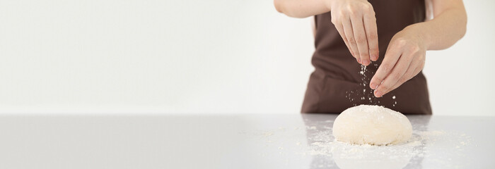 Woman Cook hands kneading sprinkling piece of fresh dough with flour on white bright kitchen table. close up on hands, horizontal Panorama cover and header web Banner. Copy space.