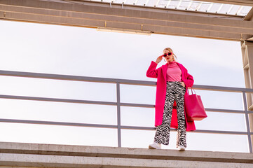 Fashionable confident blonde woman wearing trendy pink sunglasses, fuchsia color midi coat,...