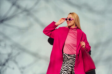 Fashionable happy smiling blonde woman wearing trendy pink sunglasses, fuchsia color coat,...