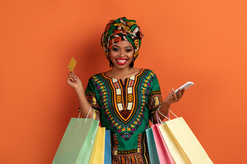 Smiling african woman shopaholic holding phone and bank card