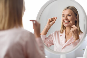 Oral Care. Middle Aged Woman Using Dental Floss Near Mirror At Home