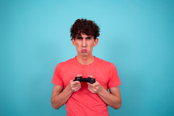 Funny young guy with a joystick in his hands. The student is playing a video game. Blue background....