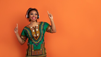 Black lady in african costume using wireless headphones, enjoying music