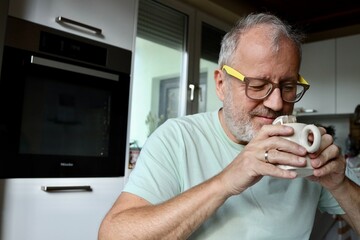 Grey haired elderly man enjoys his morning coffee in the kitchen at home 