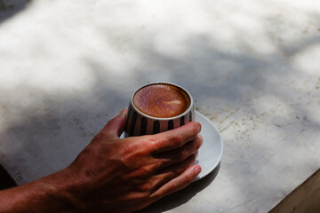 A man's hand holds a cappuccino crush on a concrete background with space for text. Stylish banner advertising coffee for breakfast. Double hot cappuccino on the background of sunlight