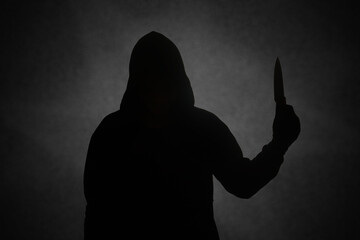 Mysterious man wearing black hoodie holding a knife to stab someone. Crimes and criminality concept