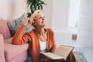 Happy mature woman sitting and reading book in living room