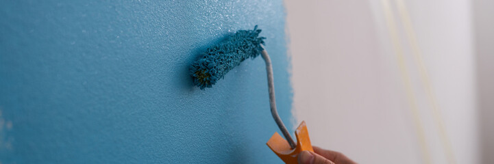Male decorator painting wall in blue color