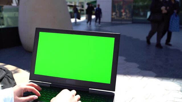 Chroma key Green screen laptop. working outside in shopping center. passing by people. Video footage mock up template 4K. Freelancer workplace