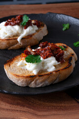 Bruschetta with dried tomato and stracciatella cheese on the black plate. Exquisite appetizer