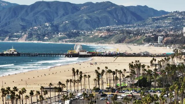 Zoomed aerial static shot of Pacific Park on the Santa Monica Pier and mountains in background. Sand beach on ocean coast. Los Angeles, California, USA