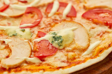 Freshly baked pizza with smoked chicken fillet and gorgonzola cheese served on wooden background with tomatoes, sauce and herbs. Food delivery concept. Restaurant menu