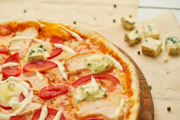 Freshly baked pizza with smoked chicken fillet and gorgonzola cheese served on wooden background with tomatoes, sauce and herbs. Food delivery concept. Restaurant menu
