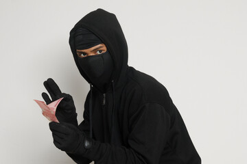 Portrait of mysterious man wearing black hoodie and mask stealing one hundred thousand rupiah...