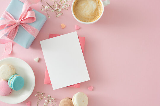 Mother's Day concept. Flat lay photo of envelope with postcard gift box cup of coffee plate with macaroons small hearts and gypsophila flowers on isolated pastel pink background with empty space