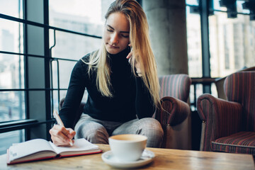 Focused woman making phone call while taking notes in planner