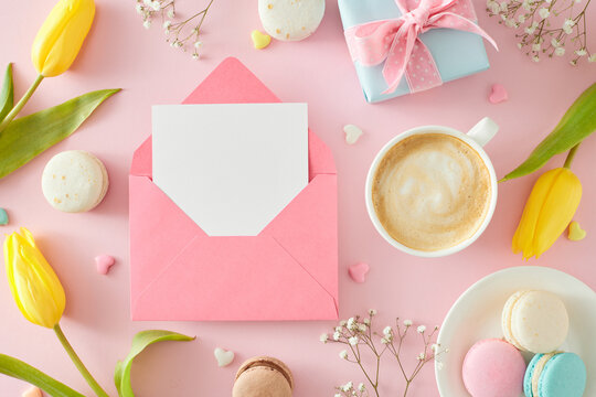 Mother's Day atmosphere concept. Top view photo of envelope with postcard gift box cup of coffee plate with macaroons hearts baubles tulips and gypsophila flowers on pastel pink background