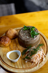 Checkered napkin, piece of meat jelly, basil, slices of garlic in white glass plate, kitchen knife and fork on wooden table